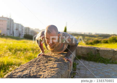 Tattooed man training outdoors doing upper body workout Tattooed man training outdoors doing upper body workout 138370801