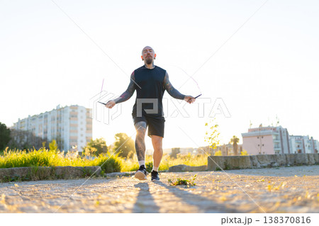 Tattooed man exercising outdoors jumping rope at sunset 138370816