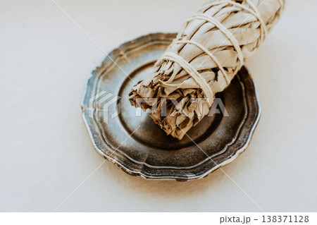 Close up of white sage bundle in ceramic dish on light background, 138371128