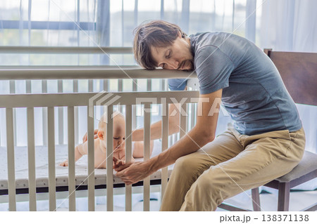 Tired father sitting by baby crib at home watching sleeping infant. Exhausted dad caring for newborn at night. Parenting fatigue, childcare responsibility, love and real family life concept Tired father sitting by baby crib at home watching sleeping infant. Exhausted dad caring for newborn at night. Parenting fatigue, childcare responsibility, love and real family life concept 138371138