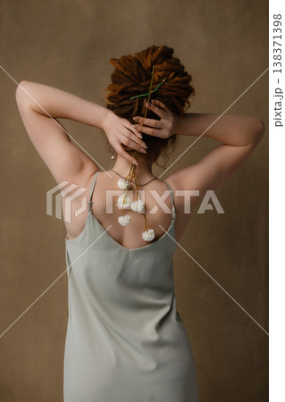 Rear view of young Caucasian woman with red dreadlocks holding dried white flowers, brown background Rear view of young Caucasian woman with red dreadlocks holding dried white flowers, brown background 138371398