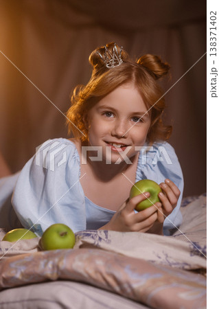 Little girl in blue dress with crown holding green apple, princess concept, studio drapery 138371402