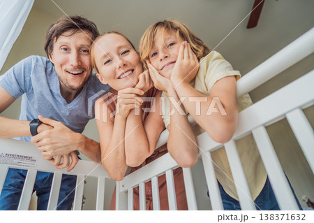 Parents and older brother looking into baby crib from infant point of view. Family smiling down at newborn with love and care. Sibling bonding, parenthood, childhood memory and connection concept Parents and older brother looking into baby crib from infant point of view. Family smiling down at newborn with love and care. Sibling bonding, parenthood, childhood memory and connection concept 138371632
