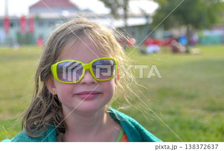 A cute little girl with sunglasses at the swimming pool. A small smiling girl in a pool towel at the swimming pool. The concept of summer, summer vacations, rest, and relaxation. A cute little girl with sunglasses at the swimming pool. A small smiling girl in a pool towel at the swimming pool. The concept of summer, summer vacations, rest, and relaxation. 138372637