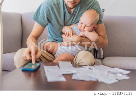 Father sitting on sofa holding baby while calculating monthly expenses with receipts at home. Stressed dad managing budget and childcare. Financial stress, parenthood and real life concept 138375115