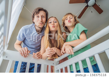 Parents and older brother looking into baby crib from infant point of view. Family smiling down at newborn with love and care. Sibling bonding, parenthood, childhood memory and connection concept Parents and older brother looking into baby crib from infant point of view. Family smiling down at newborn with love and care. Sibling bonding, parenthood, childhood memory and connection concept 138375118