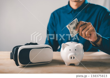 Piggy bank save future metaverse virtual digital technology reality vr, man puts cash money into ceramic bank next to headset for long term investment and online finance growth 138375813
