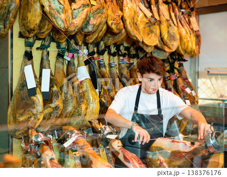 Shop assistant cutting slices from whole leg of jamon to sell in shop 138376176