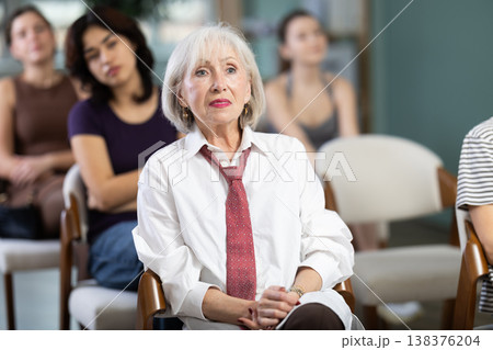 Focused mature lady with group of students different ages sitting on chairs and listening course in lecture hall 138376204