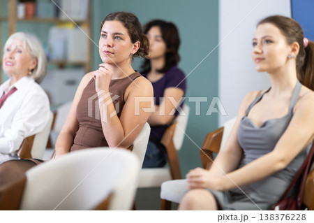 Interested group of women of different ages sitting on chairs and listening lecture in conference hall Interested group of women of different ages sitting on chairs and listening lecture in conference hall 138376228