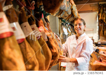 Young salesgirl working at counter of butcher shop selling Iberian jamon Young salesgirl working at counter of butcher shop selling Iberian jamon 138376341