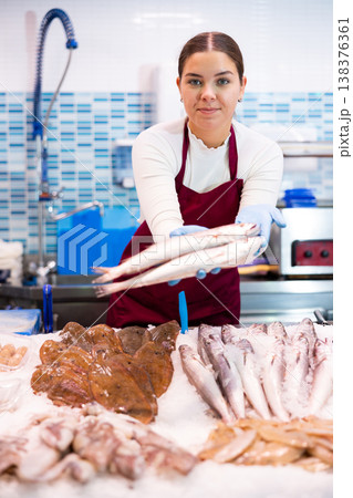 Female seller standing near counter offering fresh fish striped red mullet Female seller standing near counter offering fresh fish striped red mullet 138376361