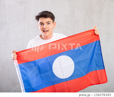 Happy young man holding flag of Laos against unicoloured background Happy young man holding flag of Laos against unicoloured background 138376385