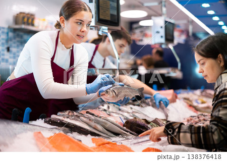 Woman seller of fish advises buyer to buy hake fresh fish Woman seller of fish advises buyer to buy hake fresh fish 138376418