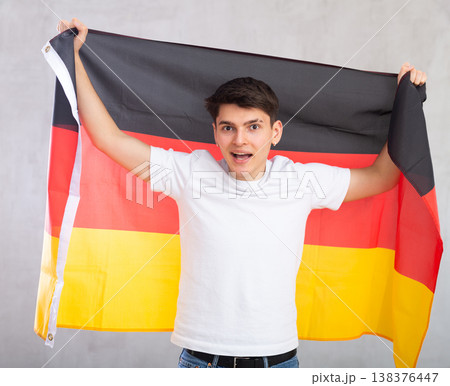 Excited, active male spectator holds national flag of Germany in hands and chants popular slogan Excited, active male spectator holds national flag of Germany in hands and chants popular slogan 138376447