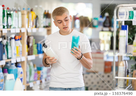 Guy buyer chooses shampoo or shower gel in household goods department of supermarket 138376490