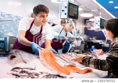 Portrait of man offering female customer fresh fish at seafood shop 138376552