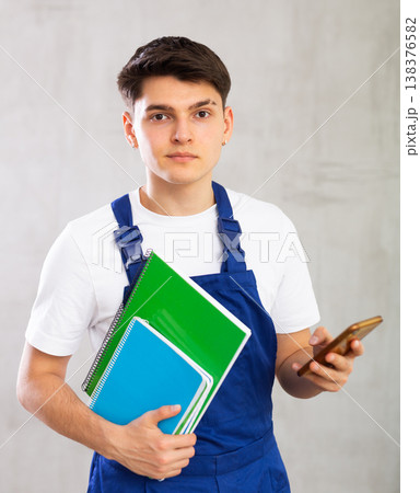Young male builder in protective overalls with notebooks in his hands writes a message on smartphone screen 138376582
