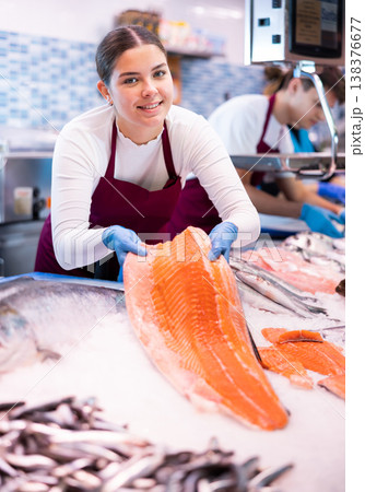 Seller in apron standing near counter offering fresh fish pink salmon 138376677