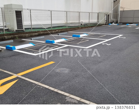 Empty automated coin parking lot in Japan with blue and white locking plate mechanisms. Numbered parking spaces on asphalt surface near a metal fence and industrial building. Professional shot. 138376831