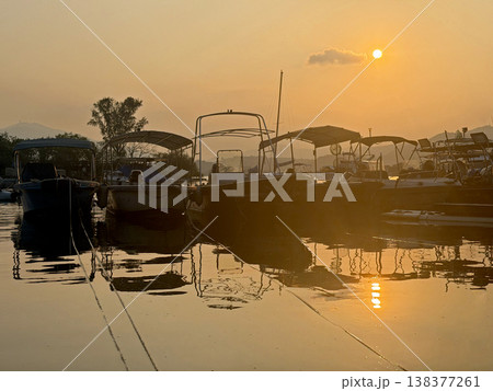 Boats docked at sunset with warm golden light reflecting on the calm water surface Boats docked at sunset with warm golden light reflecting on the calm water surface 138377261