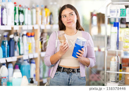 Girl selects and purchases paper cups in the household goods section of supermarket 138378446