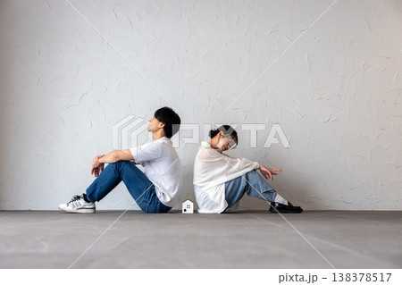 家のオブジェを真ん中にして背中合わせに座って困って考え込んでいる若い男女 家のオブジェを真ん中にして背中合わせに座って困って考え込んでいる若い男女 138378517