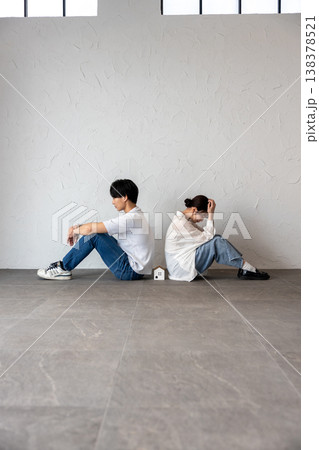 家のオブジェを真ん中にして背中合わせに座って困って考え込んでいる若い男女 家のオブジェを真ん中にして背中合わせに座って困って考え込んでいる若い男女 138378521