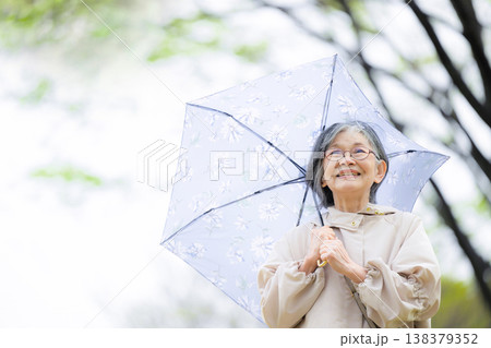 傘をさして梅雨や雨を楽しむ散歩する高齢女性の穏やかで健康的な見上げるアクティブシニアクローズアップ 138379352