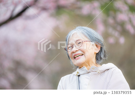 桜吹雪の桜の下で笑顔を見せる高齢女性の健康と幸せな春のイメージ お花見で桜を見上げるシニア女性 桜吹雪の桜の下で笑顔を見せる高齢女性の健康と幸せな春のイメージ お花見で桜を見上げるシニア女性 138379355