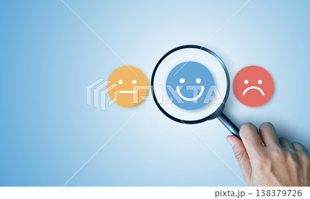 Hand holding magnifying glass focusing on happy smile face over neutral and sad icons on blue background. Concept of customer satisfaction survey, finding positive feedback and excellent service. 138379726