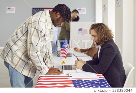 Side view portrait of a man registering at polling station with American flags on election day. 138380044