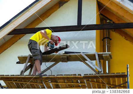 Worker bends over on platform fixing panel to house gable, house improvement project, close-up on hands and hand tool in use. 138382668
