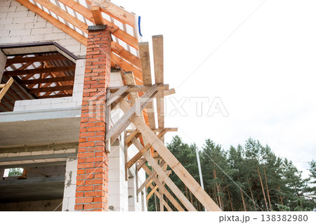 European house build, view of corner wall and open rafter frame, roof lag set ongoing, construction scaffolding apparent. European house build, view of corner wall and open rafter frame, roof lag set ongoing, construction scaffolding apparent. 138382980