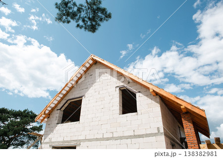 Modern house under blue sky, visible rafter lags and assembled truss structure, European construction style, roofing framework clearly shown. Modern house under blue sky, visible rafter lags and assembled truss structure, European construction style, roofing framework clearly shown. 138382981
