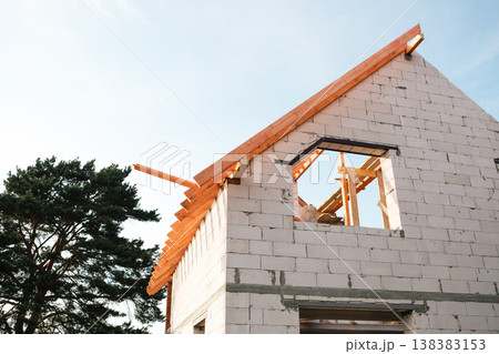 Modern white block house at step of affixing roof rafters, timber lag layout visible, credit used for home-building, financial security by insurance. 138383153