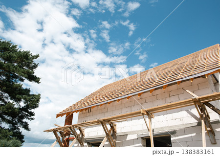 Contemporary house with erected wooden stropil system on thick masonry walls, active roofing in bright daylight, exterior design visible. Contemporary house with erected wooden stropil system on thick masonry walls, active roofing in bright daylight, exterior design visible. 138383161
