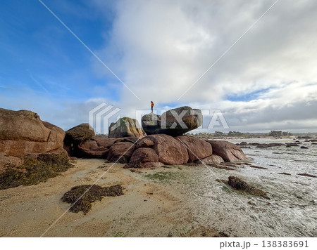 Person standing on large balancing rock in Tregastel Brittany France 138383691