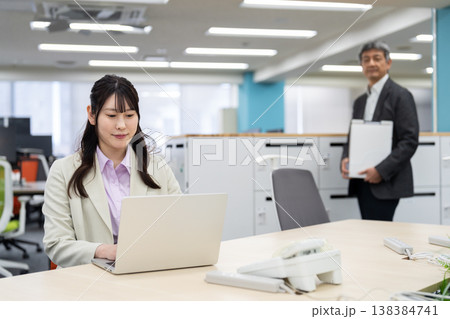 ノートパソコンで作業をする女性と背景でフリーアドレスで席を探す男性 138384741
