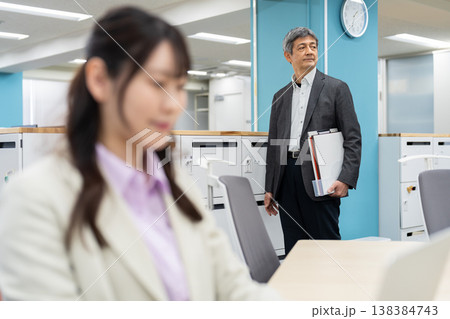 ノートパソコンで作業をする女性と背景でフリーアドレスで席を探す男性 138384743