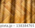 Close-up of a warm, golden oak parquet floor with diagonal light and shadow patterns 138384765