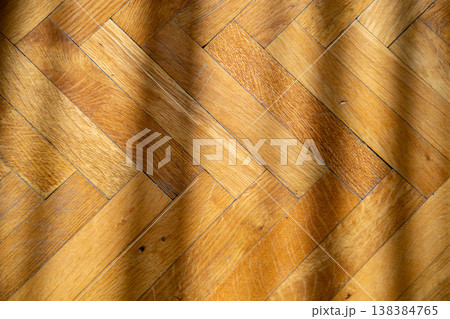 Close-up of a warm, golden oak parquet floor with diagonal light and shadow patterns 138384765