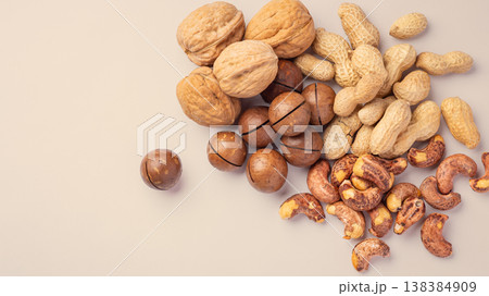 Roasted mixed nuts with nutshell, walnuts, cashews, macadamia, peanuts on light brown background, top view Roasted mixed nuts with nutshell, walnuts, cashews, macadamia, peanuts on light brown background, top view 138384909