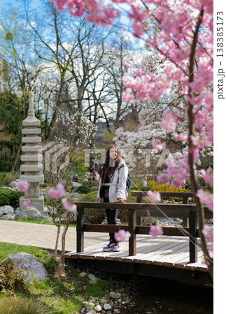 Woman enjoying cherry blossoms in a tranquil Japanese garden. Early nature awakening. 138385173