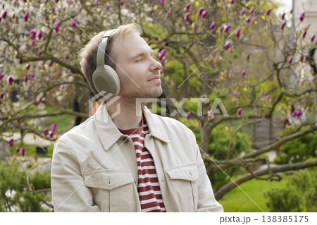 A smiling man with headphones relaxing in nature with closed eyes among blooming spring magnolia in a Japanese park A smiling man with headphones relaxing in nature with closed eyes among blooming spring magnolia in a Japanese park 138385175