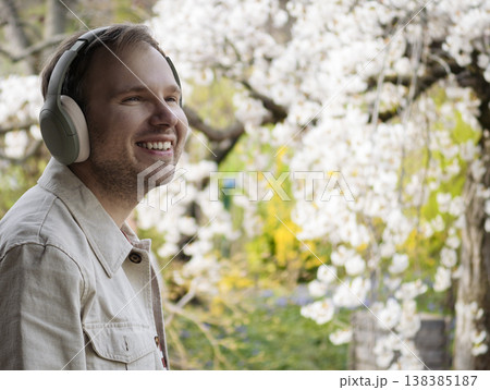 A man wearing headphones relaxes in nature among blossoming spring trees in a Japanese park, embracing a slow living moment. 138385187