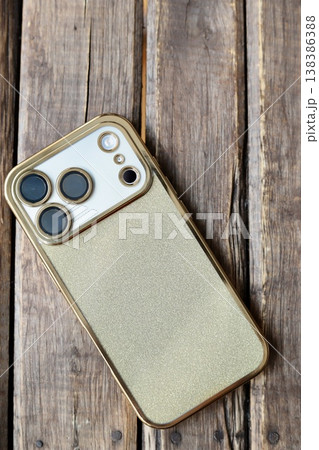ゴールドラメの背面ケースをつけた3眼カメラのスマートフォン 138386388
