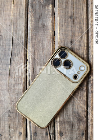 ゴールドラメの背面ケースをつけた3眼カメラのスマートフォン 138386390
