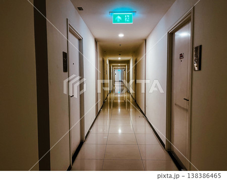 Documentary shot of a long apartment hallway with green exit sign and natural light reflection, capturing a real life everyday moment in a diverse modern family residential building at night 138386465