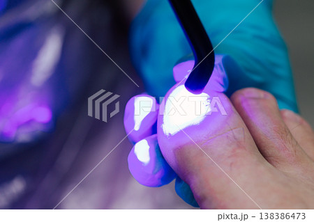 UV Lamp Curing Gel Polish on Toenail: Professional Pedicure Procedure with LED Light in Beauty Salon. Close-up view of professional pedicure procedure showing nail Bright purple light illuminates the  138386473